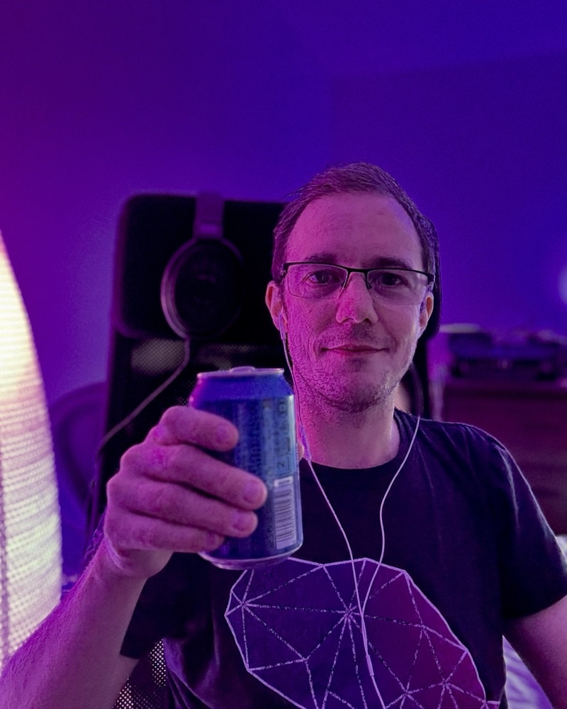 Ian, smiling in his purple-lit streaming setup, holding a drink.